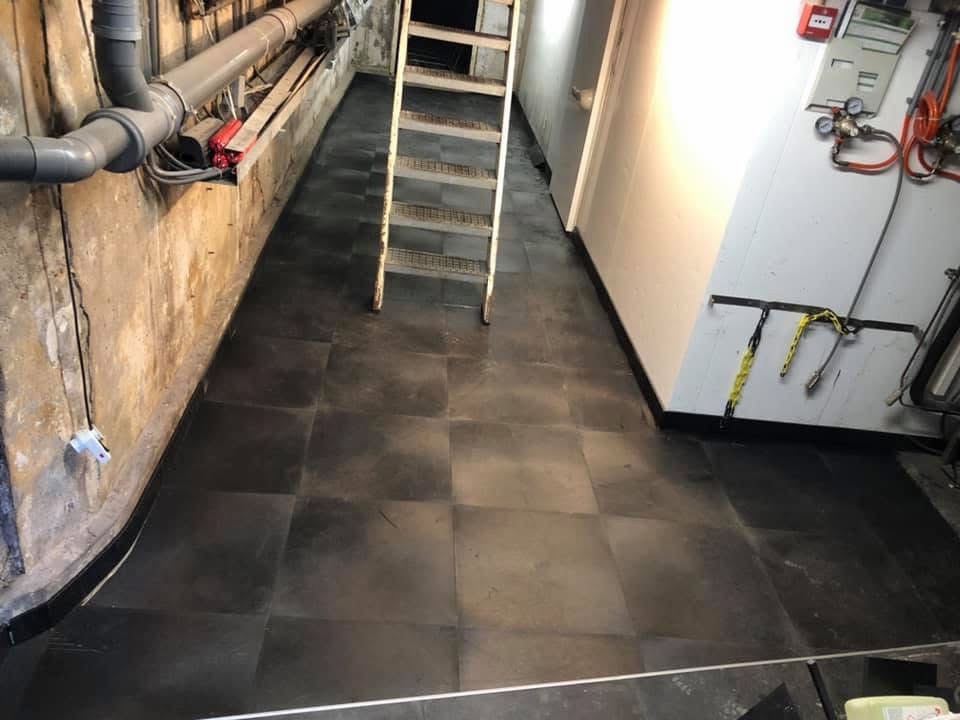 Keldervloer in Amsterdam na renovatie, bedekt met donkere PVC-bedrijfstegels